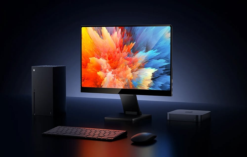 Η οθόνη Uperfect συνδεδεμένη με ένα Xbox και ένα Mac Mini, που εμφανίζει πολύχρωμα, δυναμικά γραφικά σε ένα μαύρο γραφείο.