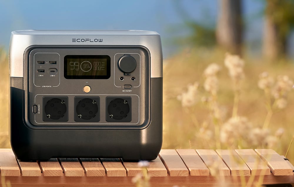 Φορητός σταθμός φόρτισης EcoFlow πάνω σε ξύλινο τραπέζι με τρεις πρίζες και οθόνη LCD σε εξωτερικό χώρο