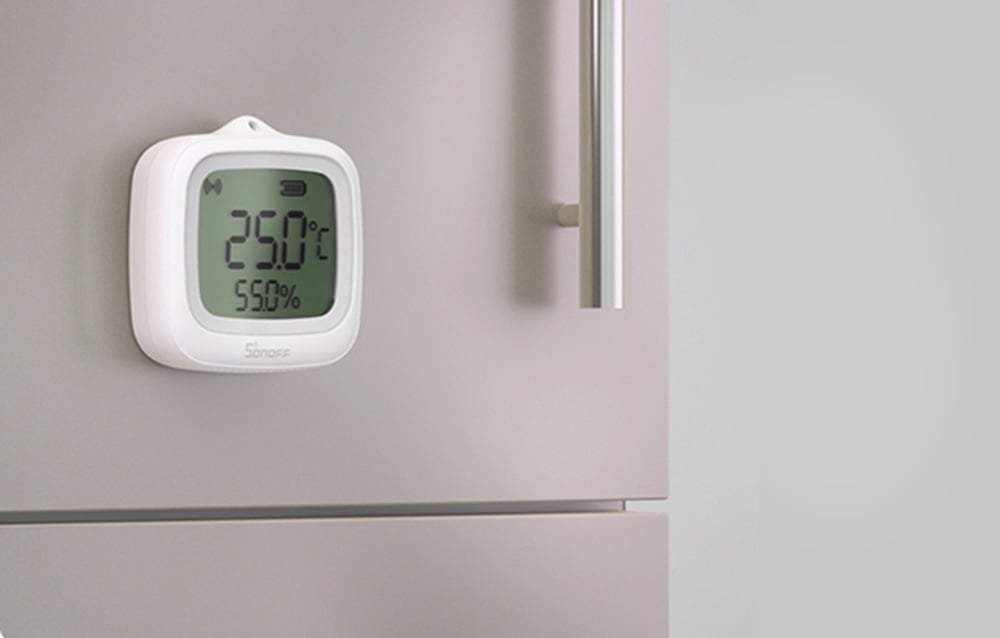 Biały cyfrowy termometr-higrometr pokazujący 29,0°C i 55,0% wilgotności zamocowany na powierzchni lodówki