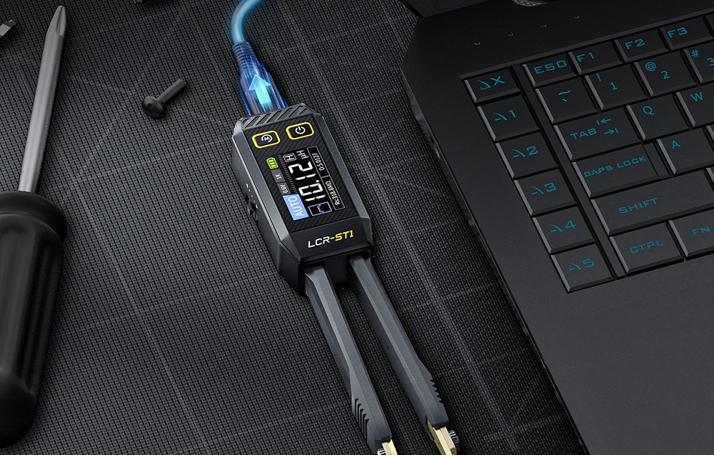 Elektroniczna pęseta pomiarowa podłączona do laptopa leży na czarnej macie obok śrubokręta i śrub.