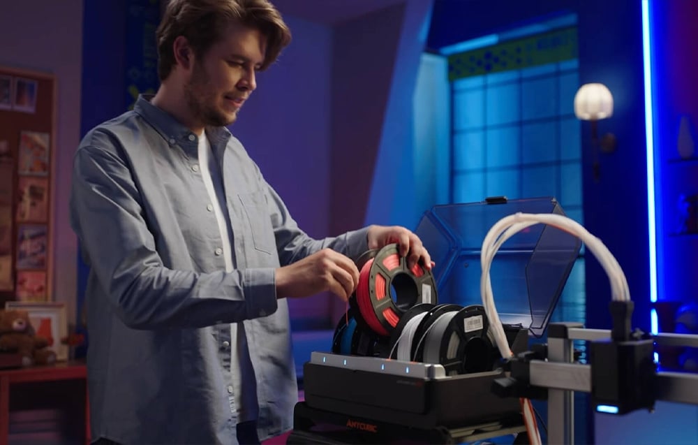 Mężczyzna w błękitnej koszuli wkładający czerwony filament do modułu ACE Pro.