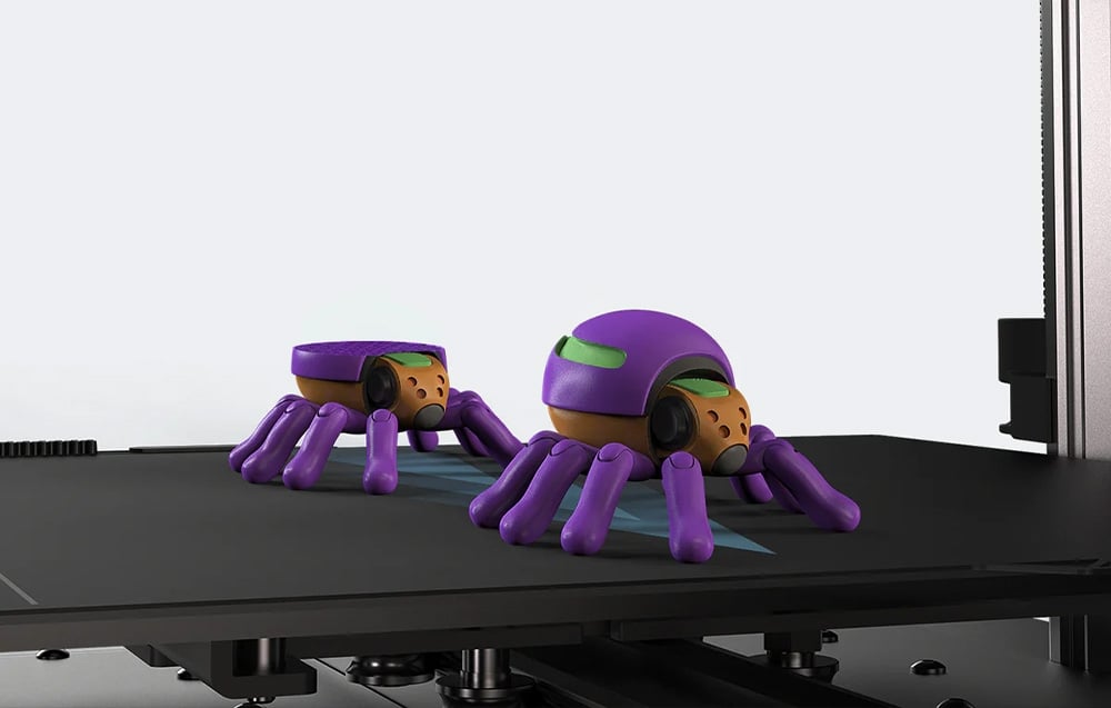 Fioletowe figurki przypominające pająki wydrukowane przez drukarkę 3D.