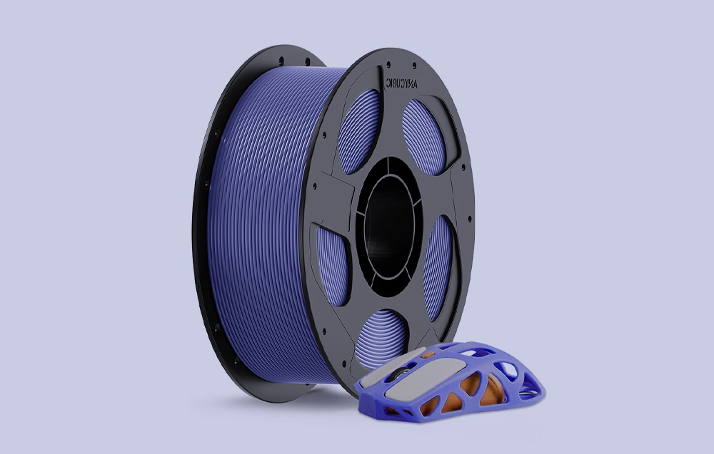 Filament w kolorze fioletowym, obok niego stoi mysz do komputera wykonana za pomocą druku 3D.