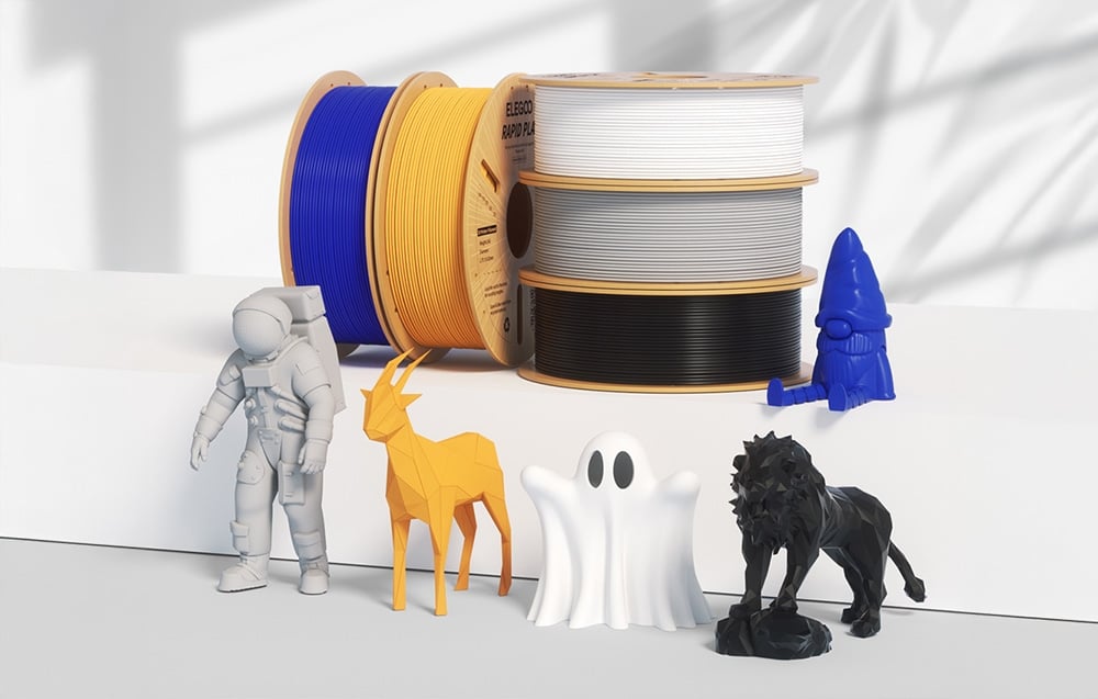 Kolorowe szpule filamentu 3D obok figurek astronauty, jelenia, ducha, rakiety i lwa