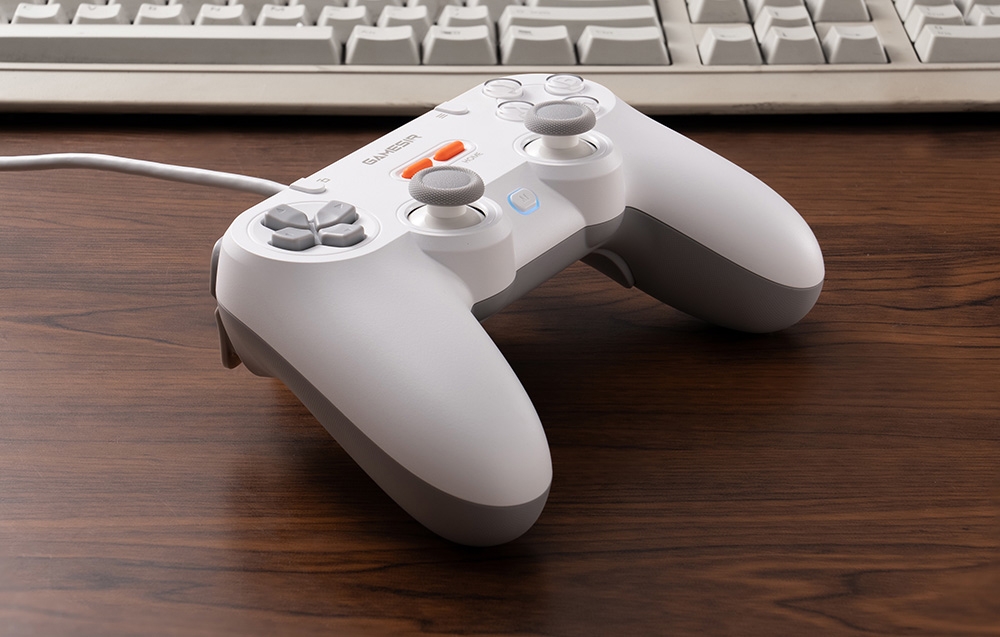 Ένα λευκό χειριστήριο GameSir, ξαπλωμένο σε ένα τραπέζι μπροστά από ένα κλασικό πληκτρολόγιο υπολογιστή.