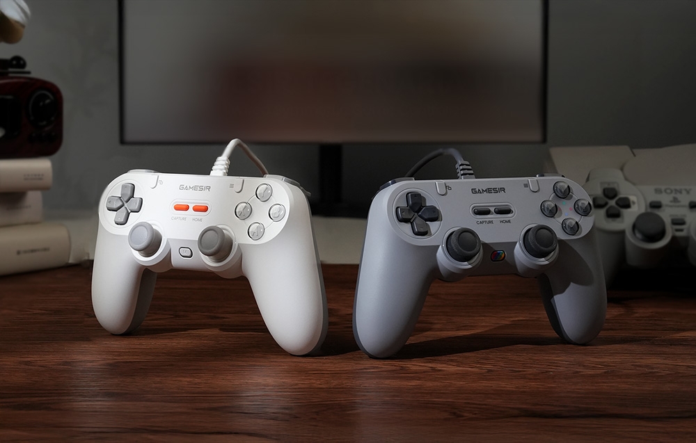Δύο ενσύρματα χειριστήρια GameSir, λευκό και γκρι, τοποθετημένα το ένα δίπλα στο άλλο πάνω σε ένα ξύλινο τραπέζι.