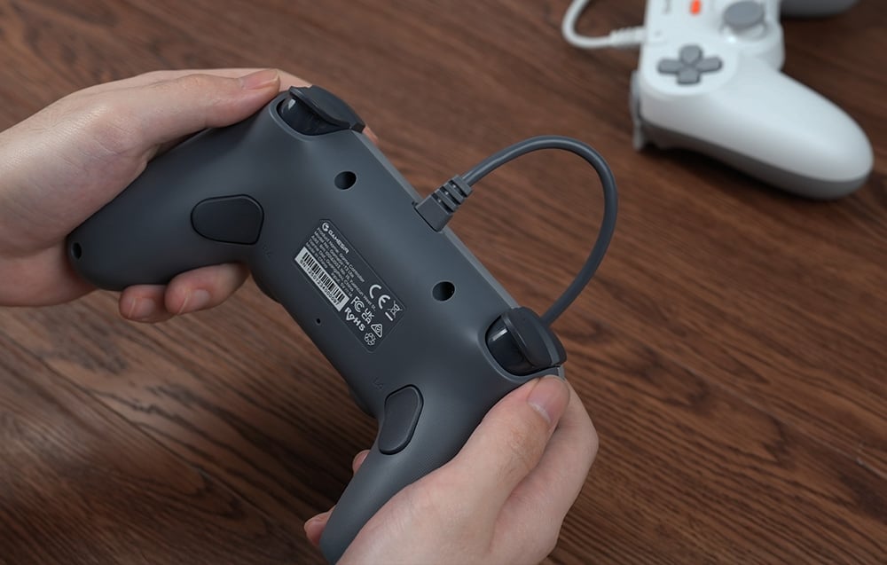 Οπίσθια όψη του γκρι χειριστηρίου GameSir που κρατείται στα χέρια με το καλώδιο συνδεδεμένο.