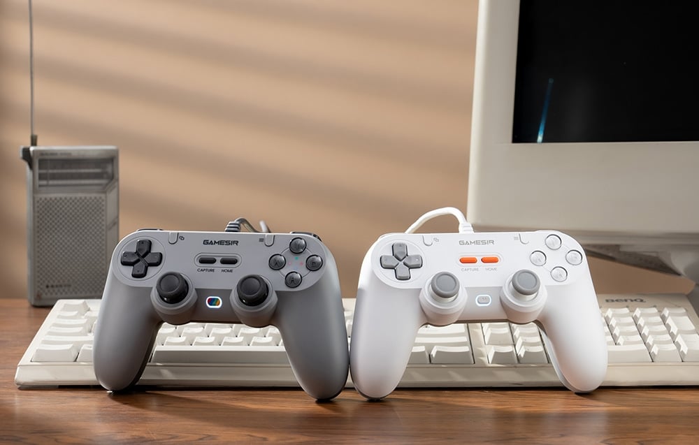 Γκρι και λευκό χειριστήριο GameSir τοποθετημένο σε πληκτρολόγιο μπροστά από οθόνη και ραδιόφωνο.
