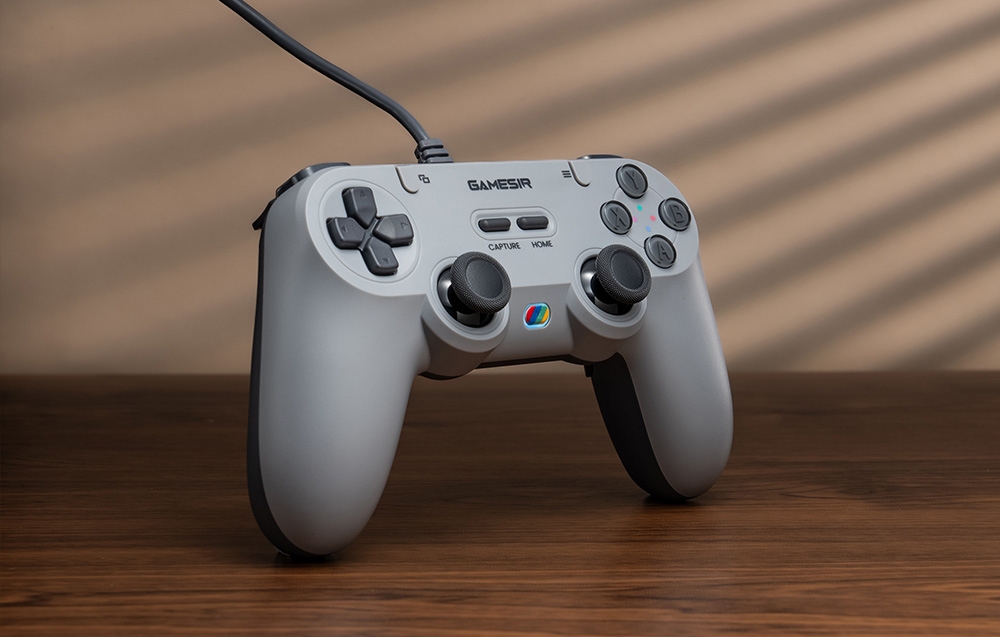 Γκρίζο χειριστήριο GameSir που στέκεται κάθετα σε ξύλινη επιφάνεια τραπεζιού με ορατά κουμπιά και οπίσθιο φωτισμό.