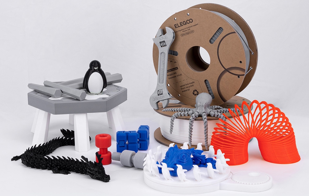biały i szary filament do drukarek 3D w otoczeniu różnych wydruków 3D