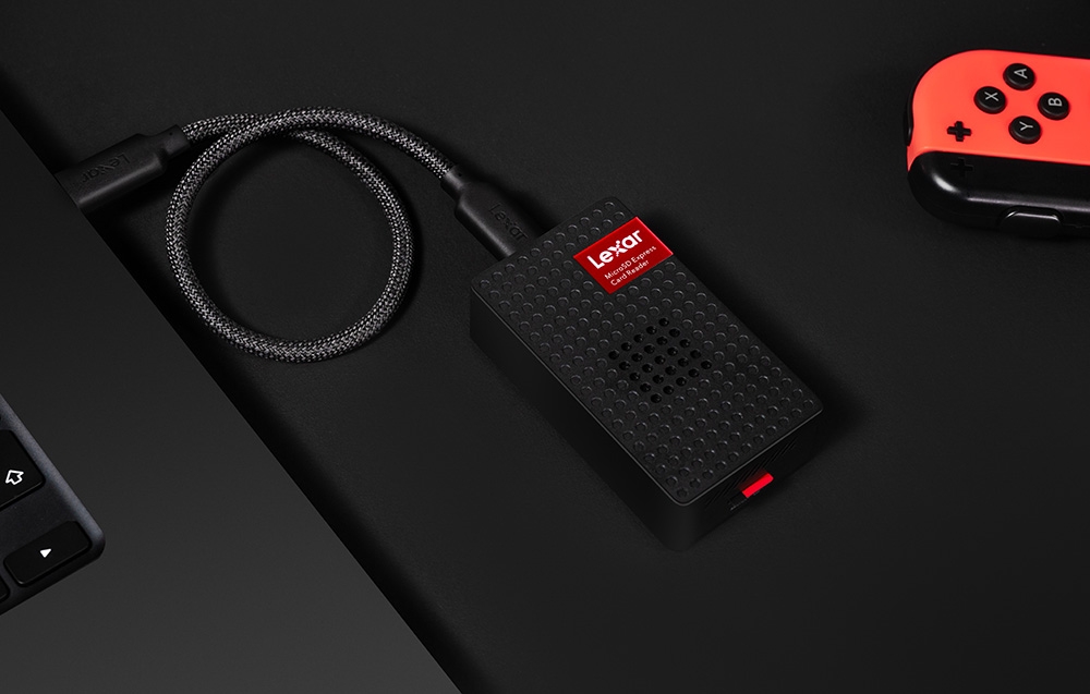Czytnik kart Lexar podłączony przewodem USB-C do laptopa, leżący na czarnym biurku obok kontrolera do konsoli
