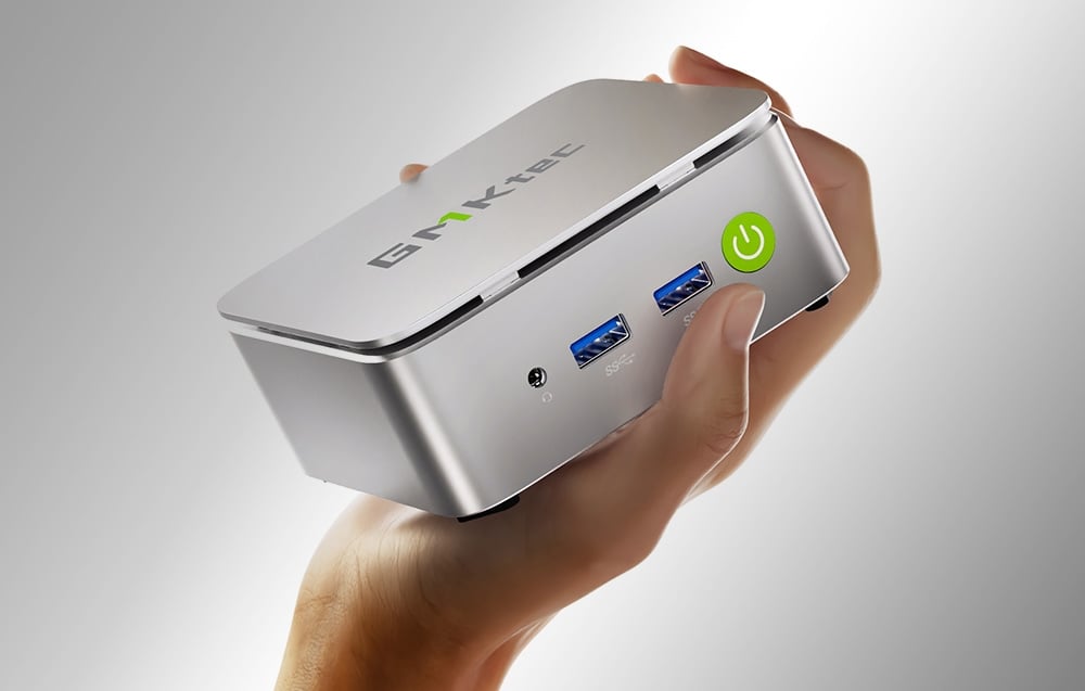 Ένα ασημένιο Mini PC κρατιέται στο χέρι με διάφορες θύρες.