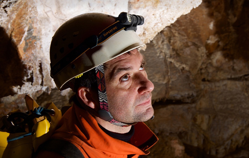 Άνδρας που φοράει κράνος ασφαλείας με φακό κεφαλής που εργάζεται σε υπόγεια σήραγγα ή σπηλιά