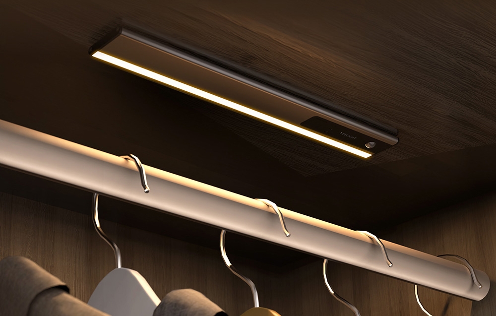 Φωτιστικό Yeelight τοποθετημένο κάτω από το ράφι στην ξύλινη ντουλάπα πάνω από τη ράβδο με τις κρεμάστρες.