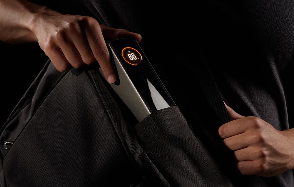 Ένας άνδρας συσκευάζει ένα powerbank με οθόνη σε ένα μαύρο σακίδιο πλάτης.