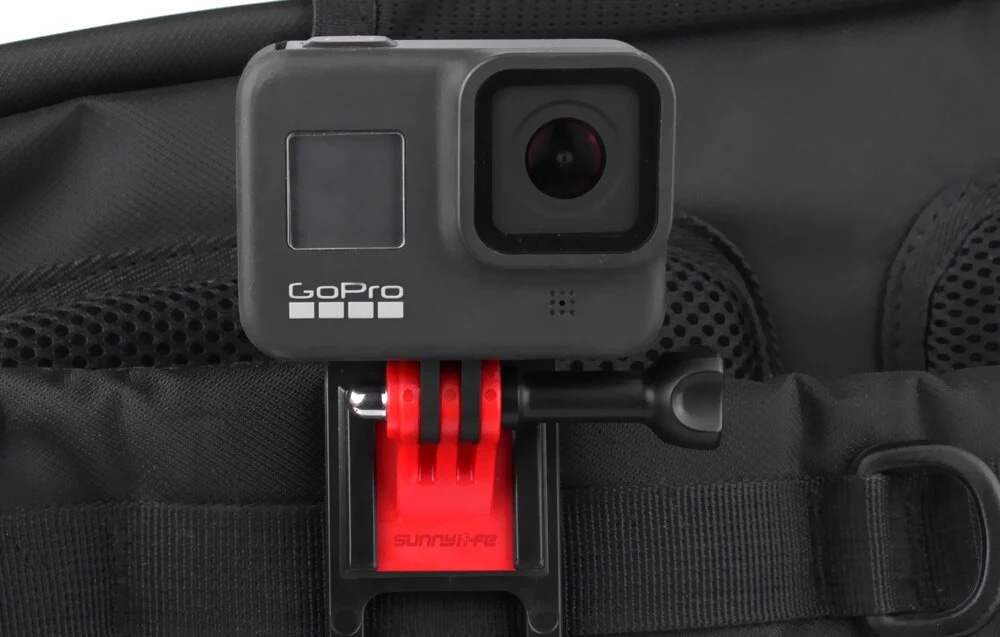Κάμερα GoPro τοποθετημένη σε κόκκινο κλιπ σε μαύρο ιμάντα σακιδίου πλάτης, μπροστινή άποψη της κάμερας