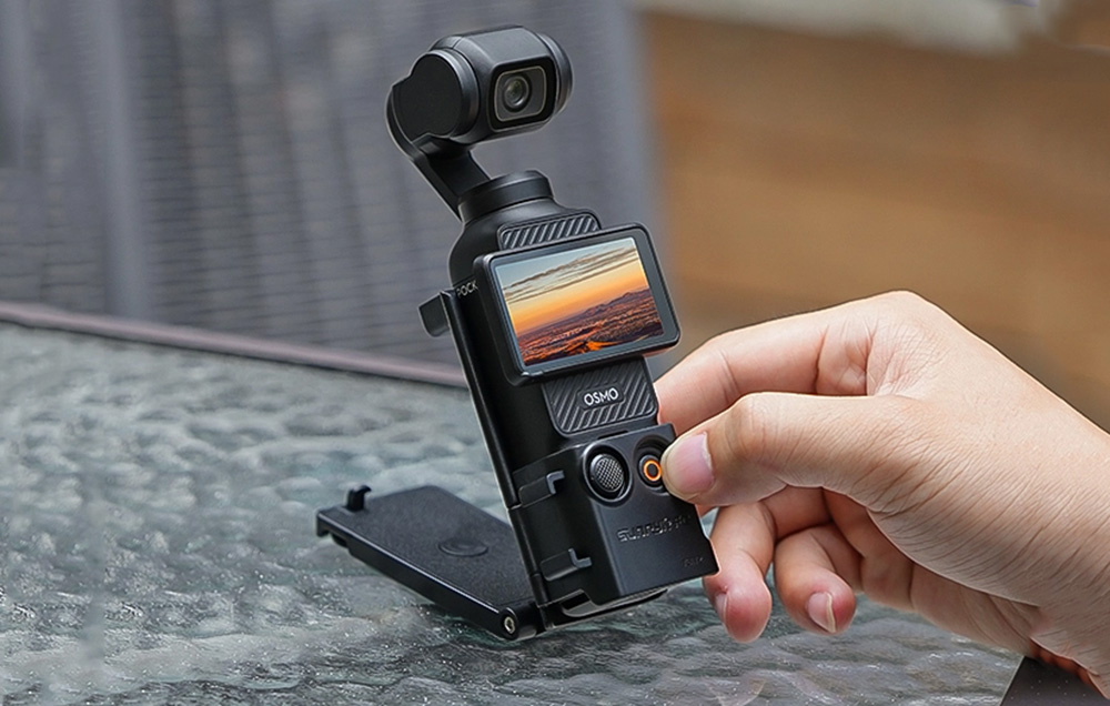 Κάμερα DJI Pocket διπλωμένη σε τραπέζι με το στήριγμα εκτεταμένο και το χέρι να φτάνει στο κουμπί