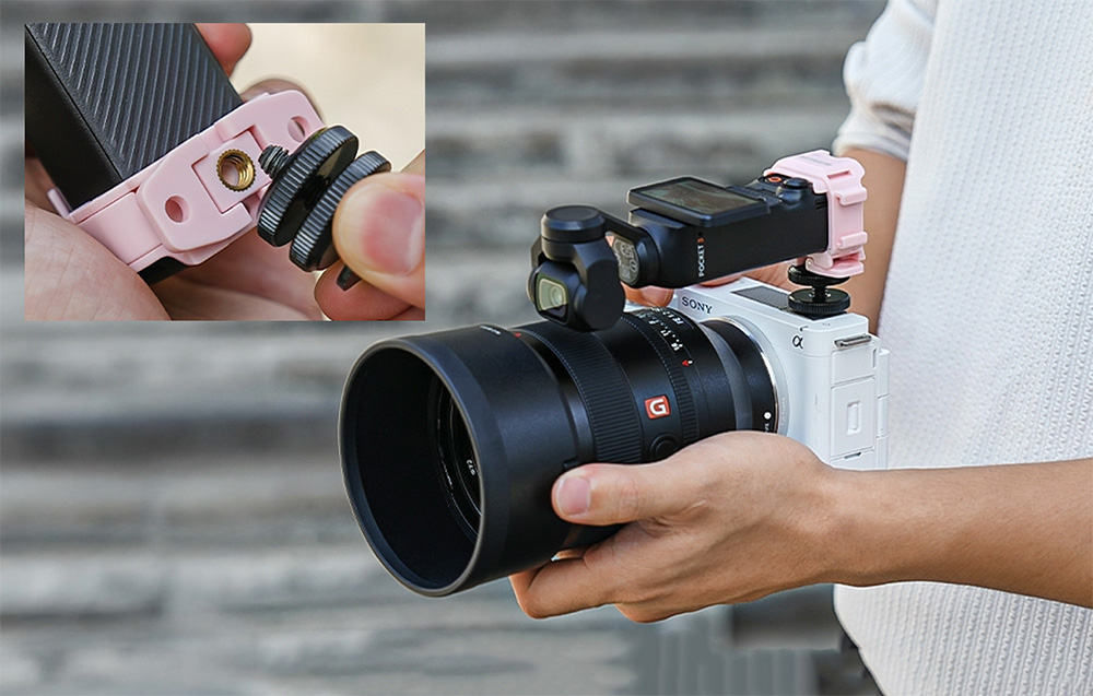 Ένα άτομο κρατάει μια φωτογραφική μηχανή Sony με μεγάλο φακό πάνω στην οποία είναι τοποθετημένη μια μικρή κάμερα DJI Pocket στο ροζ στήριγμα στήριξης