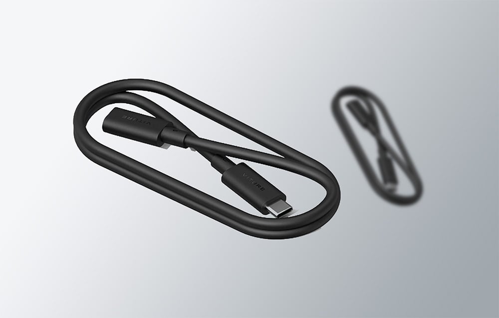 Ένα τυλιγμένο μαύρο καλώδιο USB-C της VITURE βρίσκεται δίπλα στην ασαφή αντανάκλασή του σε ένα ανοιχτόχρωμο φόντο