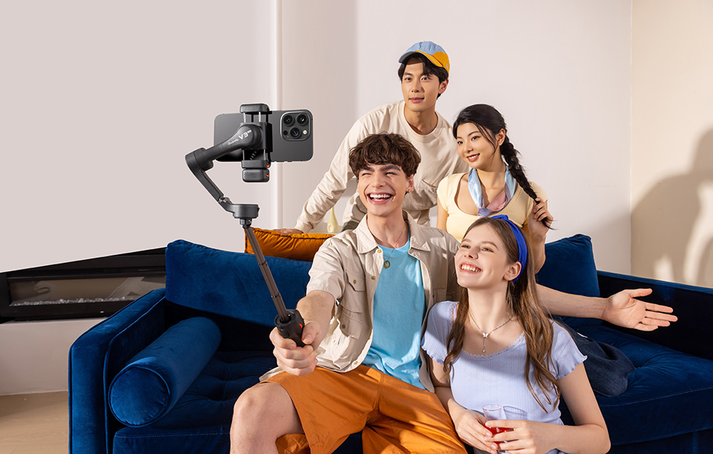 Τέσσερις νέοι βγάζουν selfie με ένα smartphone τοποθετημένο σε ένα gimbal σε ένα σαλόνι.
