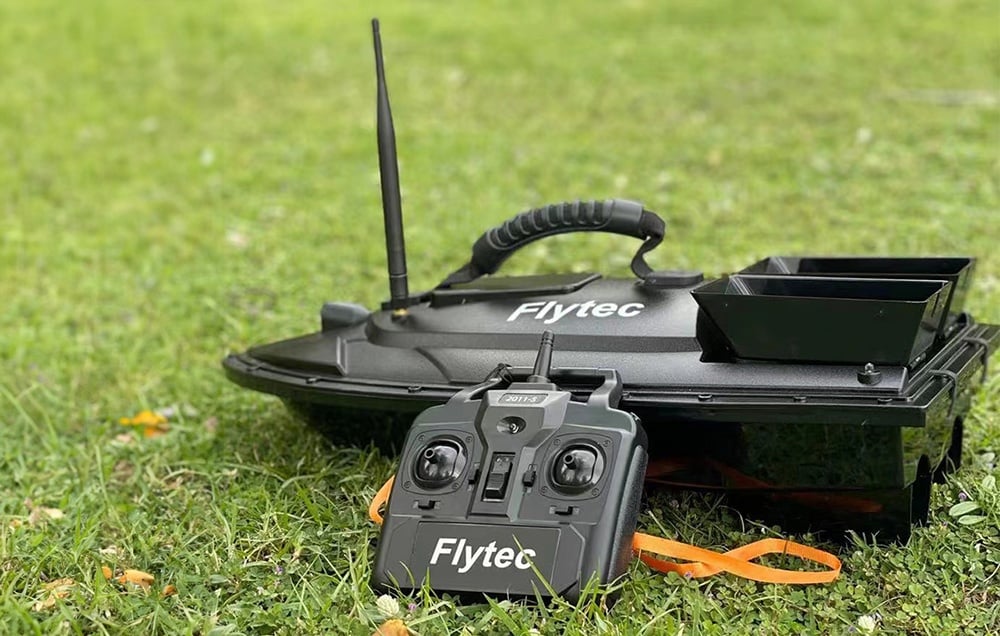 Μαύρη βάρκα δολωμάτων Flytec με τηλεχειριστήριο που βρίσκεται σε πράσινο γρασίδι