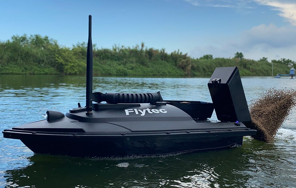Λέμβος δολωμάτων Flytec με θήκη για δολώματα που επιπλέει σε λίμνη με πράσινη ακτή στο φόντο