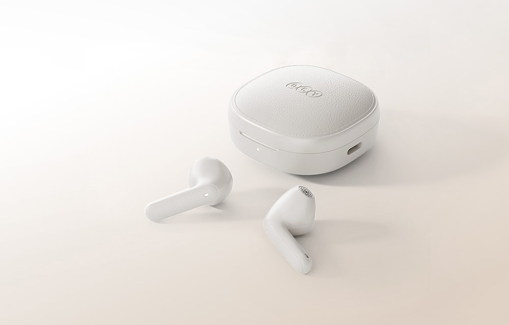 Τα ακουστικά in-ear βρίσκονται δίπλα στη θήκη φόρτισης QCY σε μπεζ φόντο.