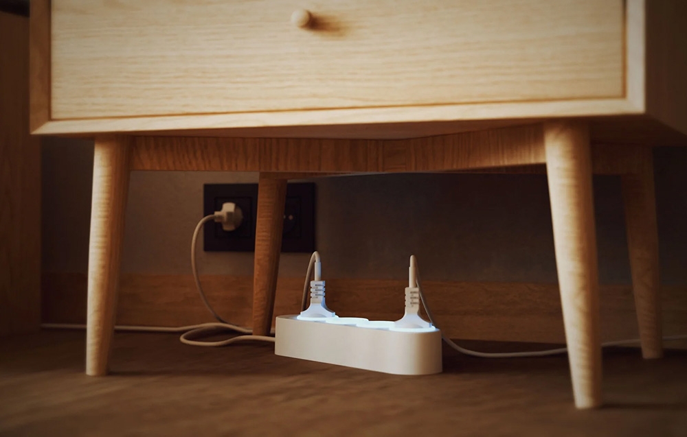 Ένα λευκό Power Strip Shelly κάτω από ένα ξύλινο κομοδίνο με δύο συνδεδεμένες συσκευές