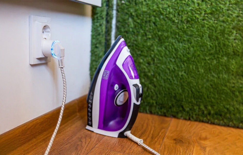 Shelly Plug S με μπλε φωτισμό συνδεδεμένο σε σίδερο δίπλα σε τοίχο με τεχνητό γρασίδι