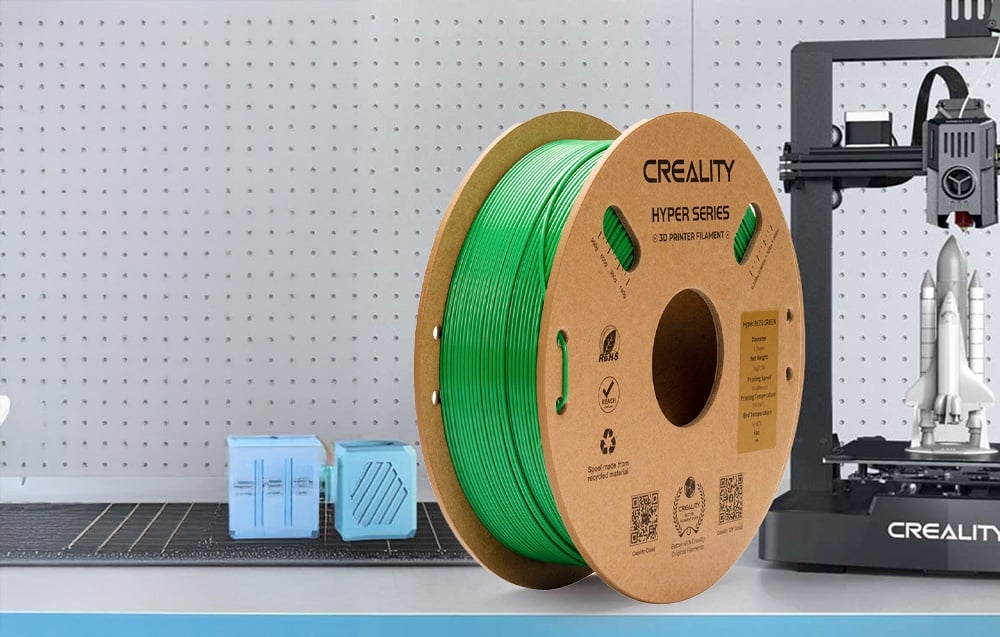 Καρούλι με πράσινο νήμα δίπλα σε εκτυπωτή 3D και μπλε μοντέλα