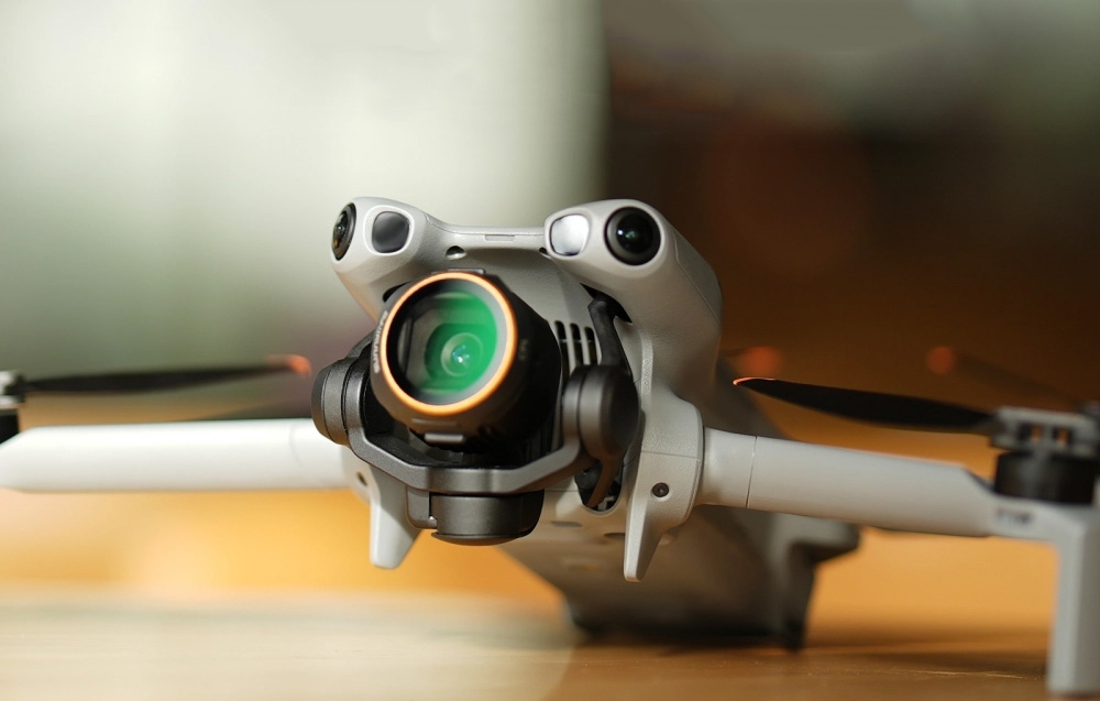 Drone με ασημί σώμα και κάμερα με gimbal, πράσινο φακό και χρυσό δακτύλιο πάνω σε ξύλινο τραπέζι