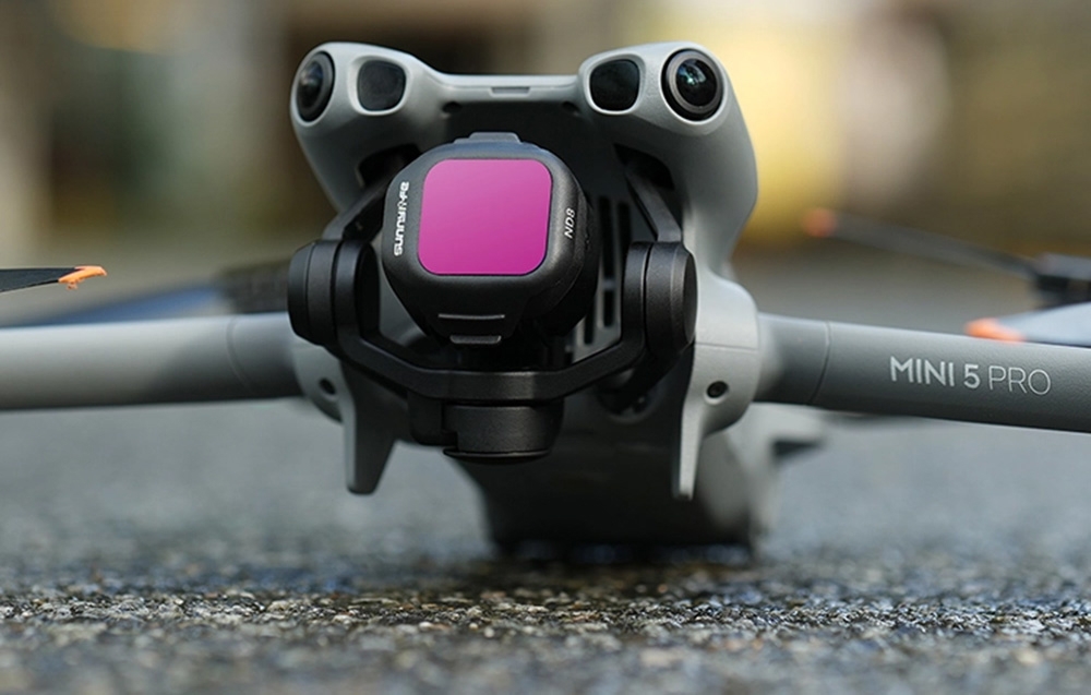 Drone DJI Mini 5 Pro με το ροζ φίλτρο τοποθετημένο στην κάμερα, μπροστινή όψη στο έδαφος