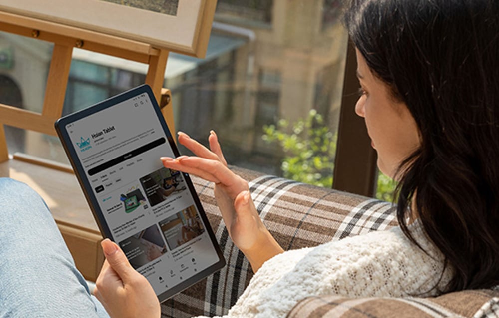 Γυναίκα που περιηγείται στον ιστότοπο Huion Tablet σε tablet, καθισμένη αναπαυτικά δίπλα στο παράθυρο