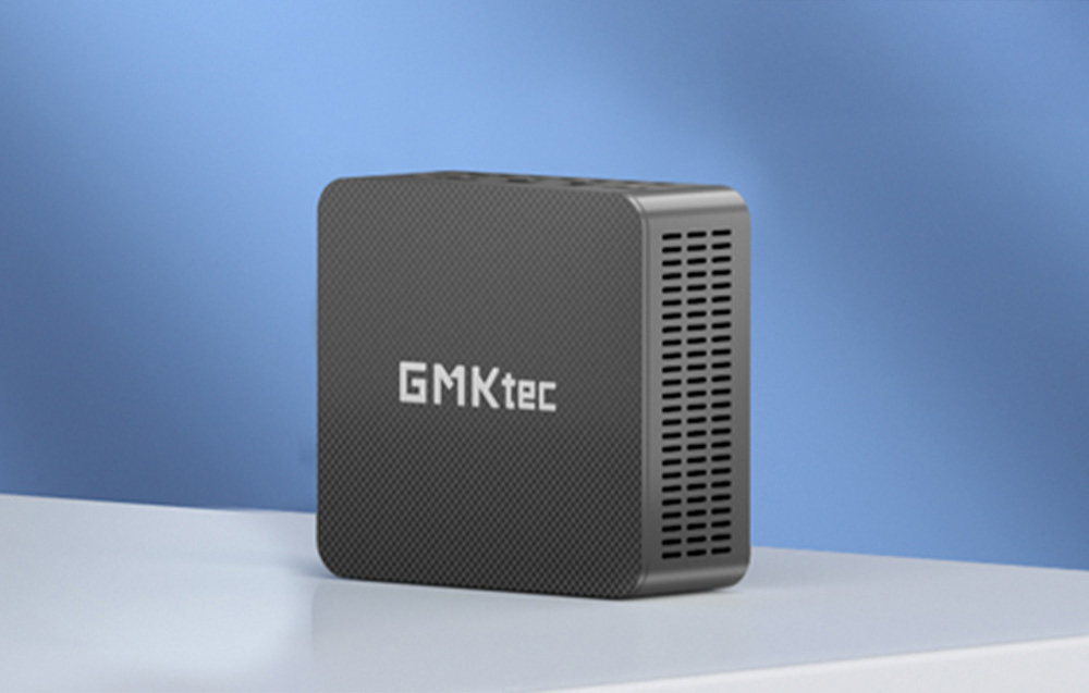Μαύρος μικροϋπολογιστής GMKtec με εμφανές λογότυπο στην πρόσοψη, τοποθετημένος σε φωτεινή επιφάνεια σε μπλε τοίχο