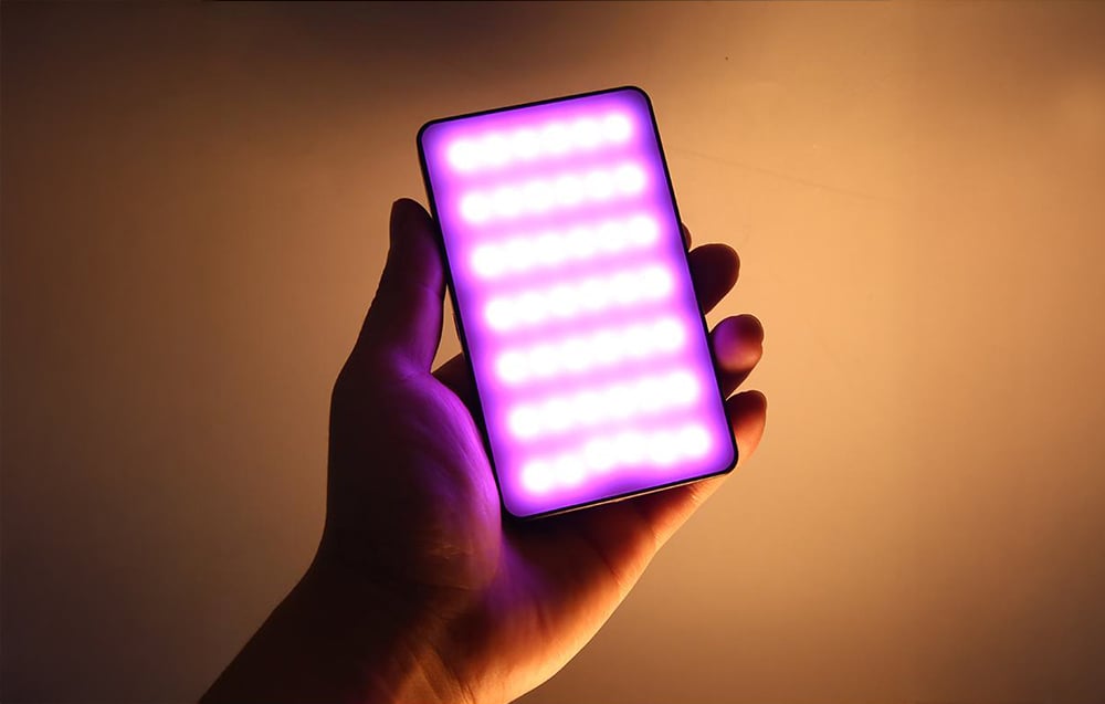Ο συμπαγής λαμπτήρας LED RGB PULUZ που κρατάτε στο χέρι λάμπει με μοβ και πορτοκαλί φως, παρουσιάζοντας χρωματικά εφέ