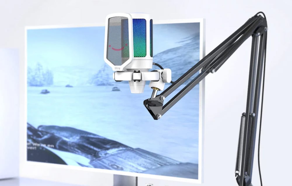 Λευκό μικρόφωνο με pop filter σε τρίποδο, στο βάθος οθόνη στο γραφείο