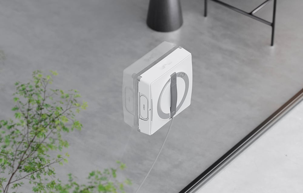 Το ρομπότ καθαρισμού παραθύρων Ecovacs W2 Pro Omni πλένει το τζάμι του παραθύρου, στα αριστερά μπορείτε να δείτε ένα κομμάτι του φυτού.