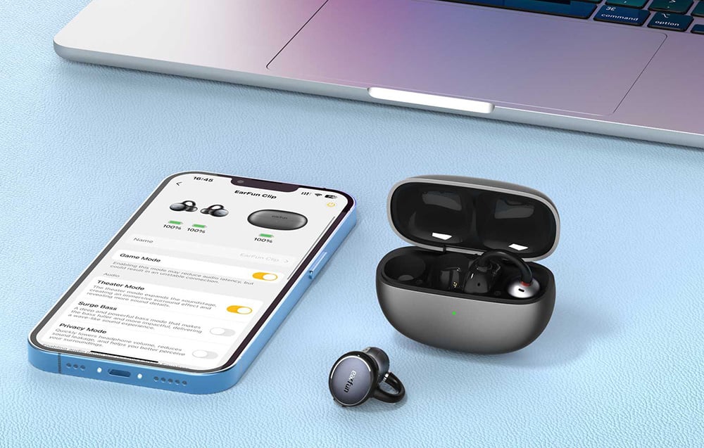 Μαύρα ακουστικά EarFun Clip, smartphone και φορητός υπολογιστής σε ανοιχτόχρωμο τραπέζι
