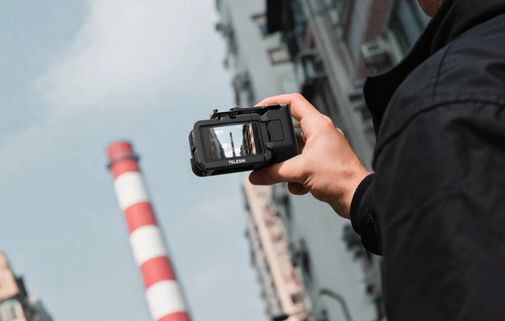 Ένα χέρι κρατάει μια κάμερα DJI σε ένα μαύρο περίβλημα Telesin με φόντο μια βιομηχανική καμινάδα