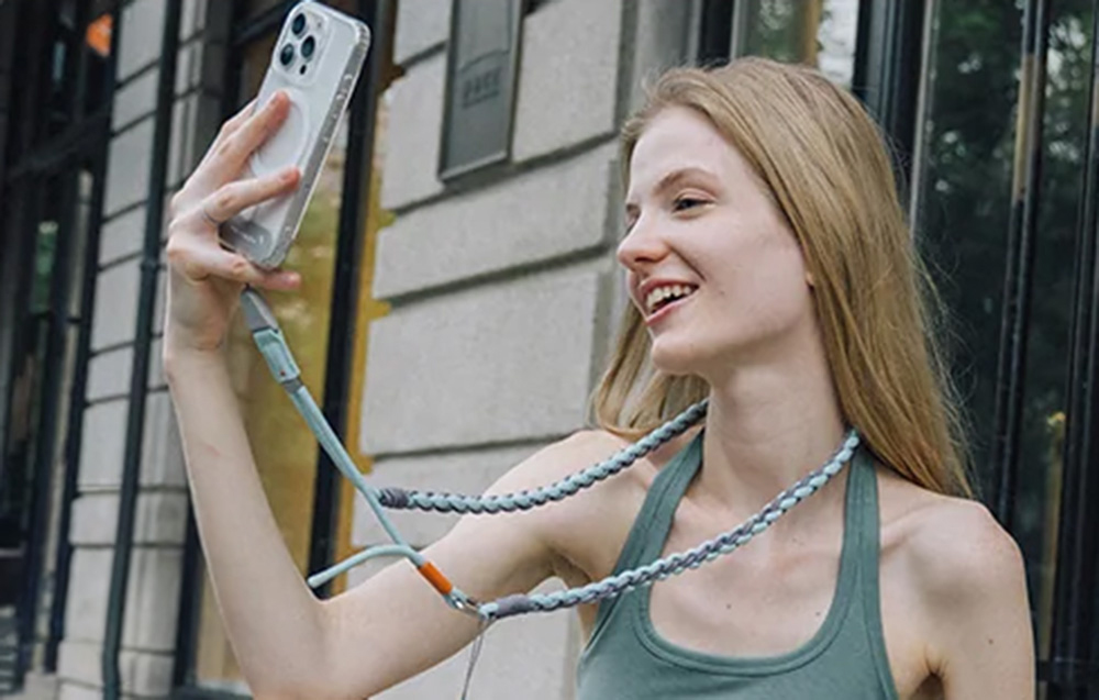 Μια ξανθιά γυναίκα βγάζει selfie με το smartphone της συνδεδεμένο με έναν ιμάντα PGYTECH