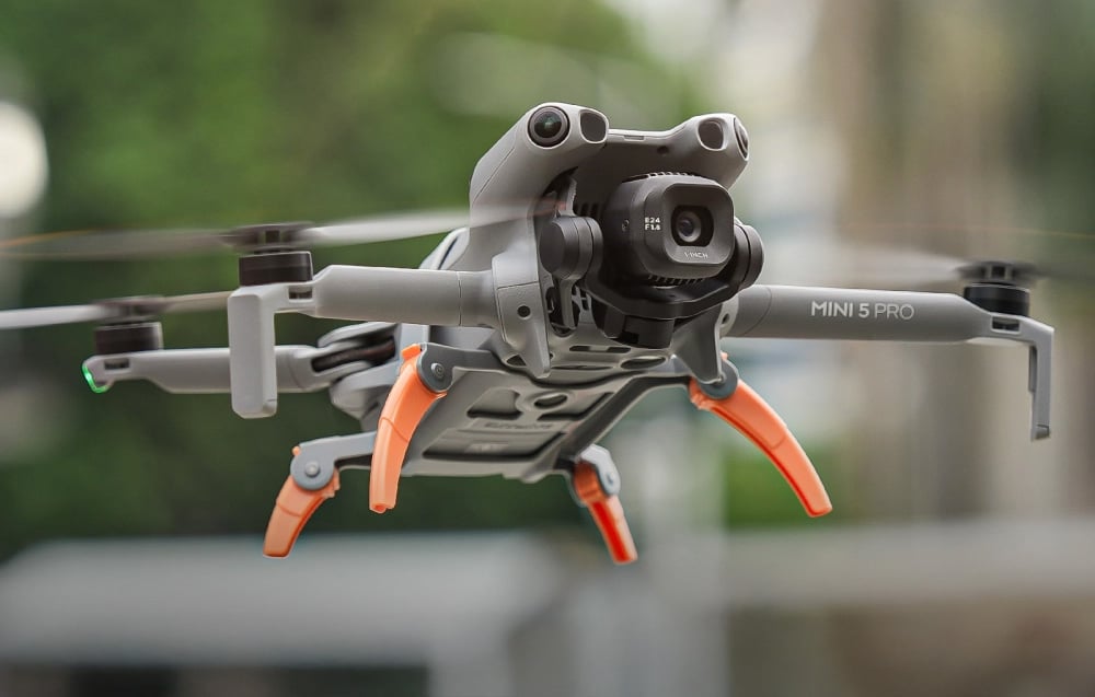 Ιπτάμενο drone DJI Mini 5 Pro με πορτοκαλί πόδια απλωμένα, αιωρούμενο στον αέρα