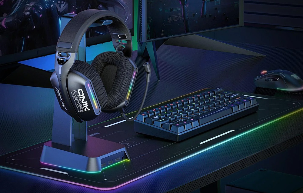 Ακουστικά gaming κρεμασμένα σε βάση δίπλα σε πληκτρολόγιο, ποντίκι και δύο οθόνες