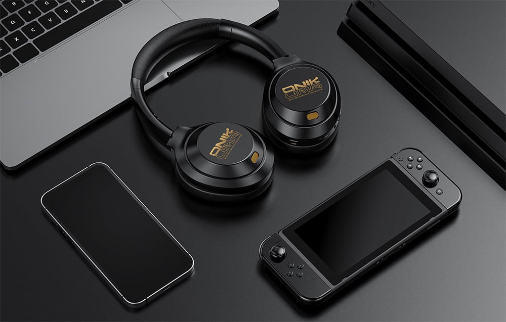 Μαύρα ακουστικά in-ear που βρίσκονται πάνω σε έναν φορητό υπολογιστή δίπλα σε ένα smartphone και μια κονσόλα κινητής τηλεφωνίας