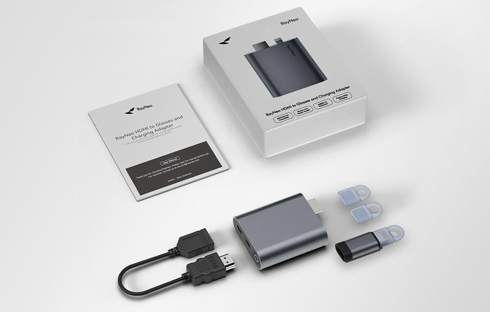 Σετ RayNeo με προσαρμογέα, αντάπτορες, καλώδιο HDMI και οδηγίες, τοποθετημένα δίπλα στη συσκευασία σε φωτεινό φόντο.