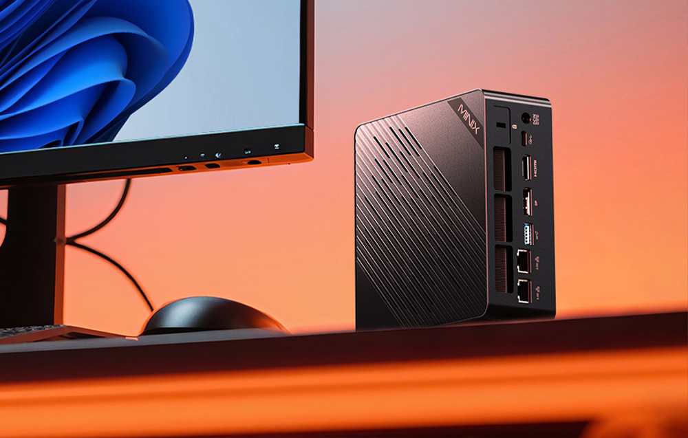 Mini PC MINIX τοποθετημένο κάθετα σε ένα γραφείο δίπλα σε μια οθόνη, με ορατές θύρες στο πίσω μέρος του περιβλήματος.