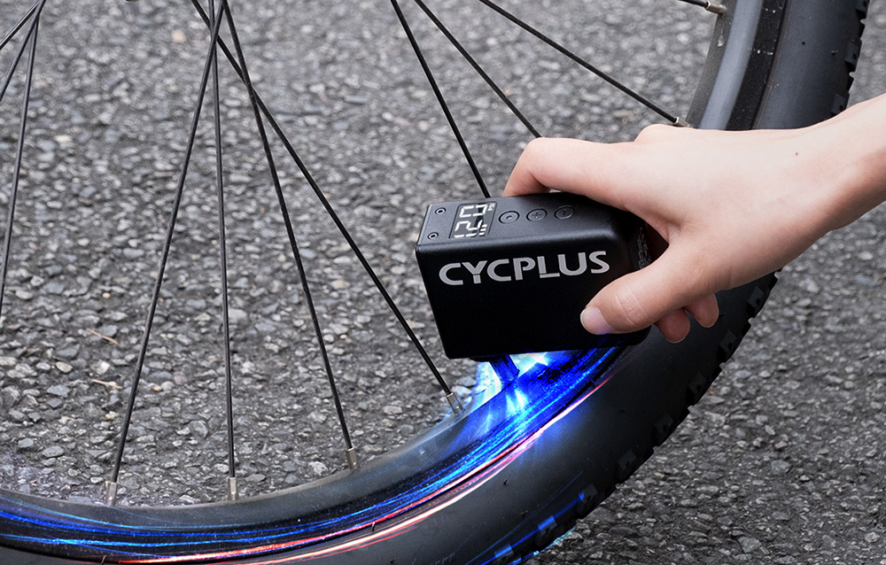 Χέρι που κρατάει τον φουσκωτή Cycplus με μπλε φως στον τροχό του ποδηλάτου