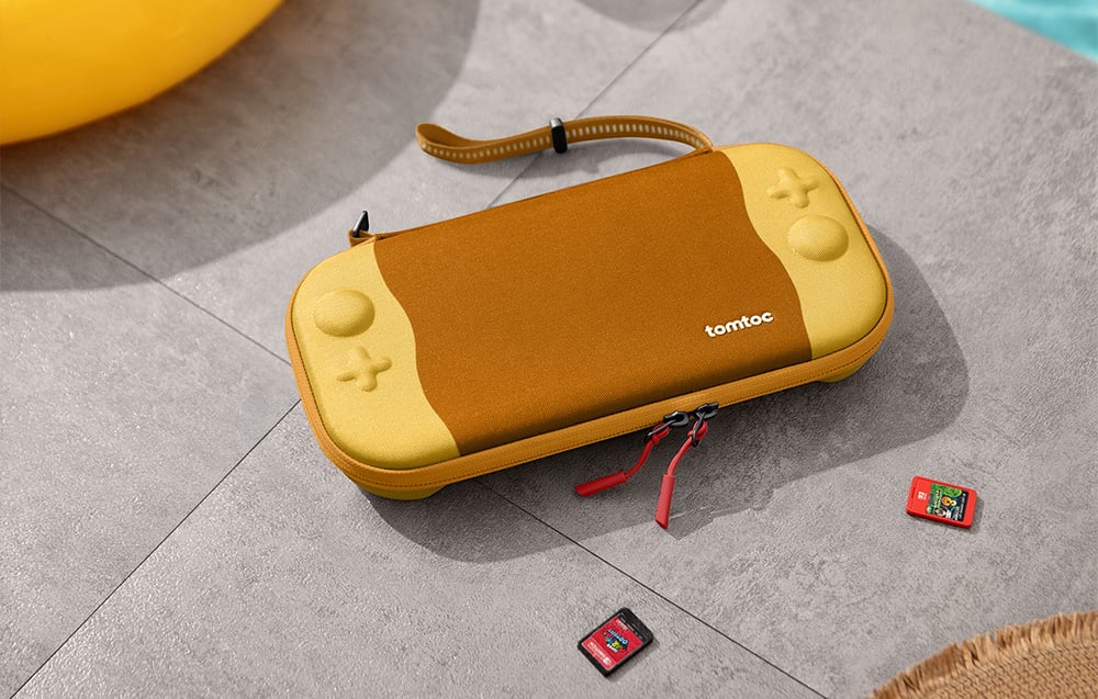 Κίτρινη θήκη κονσόλας Nintendo Switch σε γκρι πλακάκια δίπλα σε κάρτες