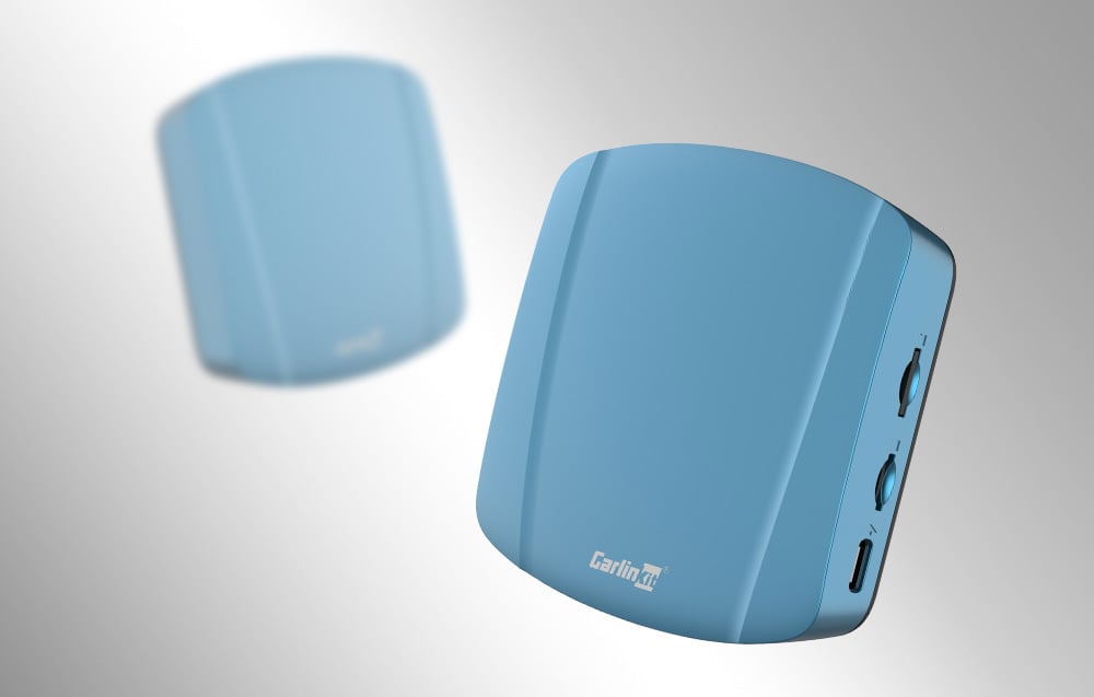 Δύο ασύρματοι προσαρμογείς Carlinkit TBOX ULTRA, σε ανοιχτόχρωμο φόντο, ο ένας θολωμένος.