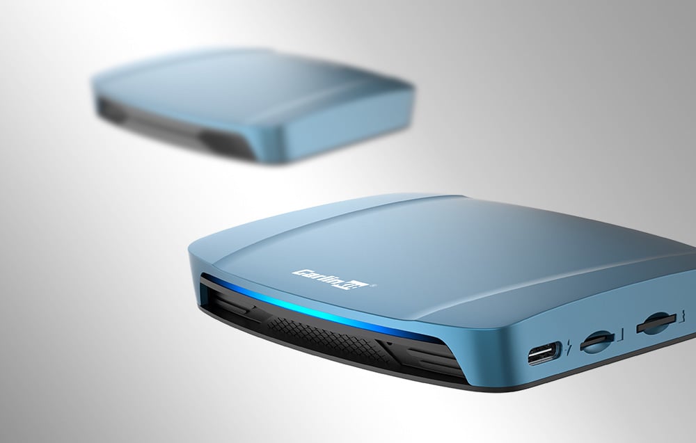 Δύο ασύρματοι προσαρμογείς Carlinkit TBOX ULTRA, σε ανοιχτόχρωμο φόντο, ο ένας θολωμένος.