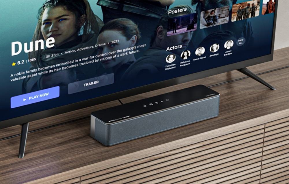 Soundbar τοποθετημένο σε ξύλινο ράφι κάτω από τηλεόραση που προβάλλει πλατφόρμα streaming